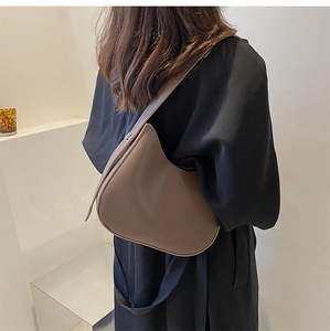 Modern brown crescent hobo bag shown on shoulder in a minimalist urban setting