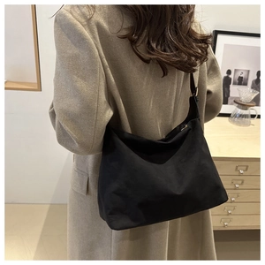 Detailed view of the large black suede tote bag styled with a beige wool coat in a warm room