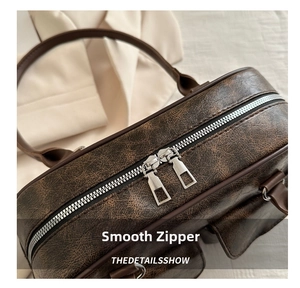 Dettaglio delle doppie cerniere in metallo su borsa vintage marrone con trama in pelle opaca