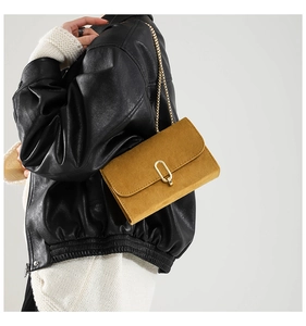 Détail du sac à rabat en daim jaune moutarde avec chaîne dorée sur une veste en cuir noir