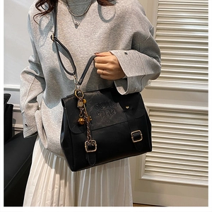 Close-up of black leather crossbody bag featuring letter embossing and golden metal buckle