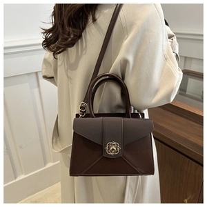 Detail of dark brown leather handbag featuring a golden four-leaf clover buckle and top handle