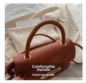 Detailed macro of brown leather handbag featuring pebble grain texture and gold metal clasp