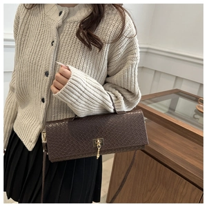 Detail of dark brown faux crocodile texture handbag with golden lock and key charm