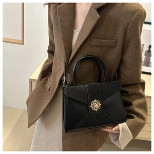 Detail of minimalist black leather handbag with vintage gold floral buckle on suit