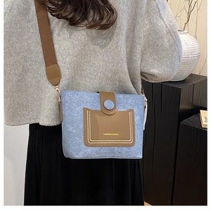 Detail of blue denim and brown leather crossbody bucket bag with pearl stud accents