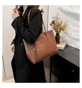 Detail view of large vintage brown tote bag with woven charm on a shoulder strap