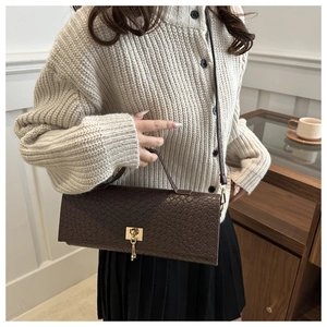 Close-up of dark brown crocodile texture handbag featuring a vintage gold lock and key charm