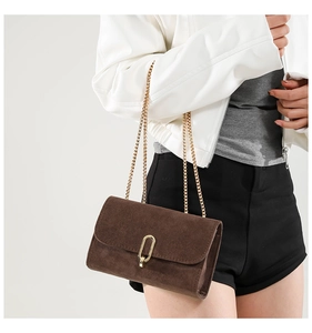 Gros plan du sac bandoulière en daim marron avec boucle dorée et fine chaîne