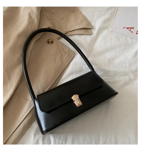 Détail du sac sous le bras vintage noir avec boucle dorée sur un tissu blanc