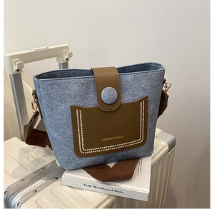 Detail of blue denim bucket bag with brown leather accents on a white suitcase