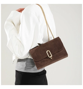 Détail d'un sac bandoulière en daim marron foncé avec fermoir doré et bandoulière chaîne