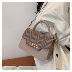 Detail of elegant beige crossbody bag with woven flap and golden metal clasp on a wooden table