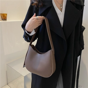 Minimalist brown crescent shoulder bag in PU leather with wide strap worn with trench coat