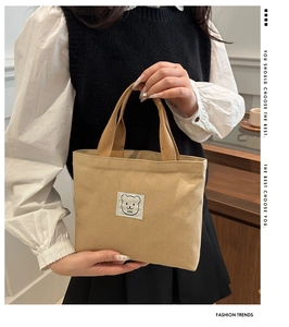 Detail view of khaki canvas tote bag featuring a cute cartoon bear patch and soft texture
