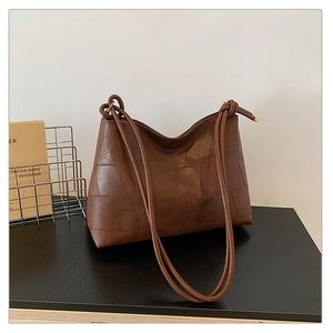 Macro detail of dark brown patchwork leather tote bag with geometric stitching on table