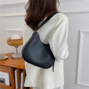 Minimalist black leather underarm bag in a sleek half-moon silhouette on a model shoulder
