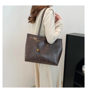 Detail of dark brown tote bag showing leather texture and gold bell charm pendant