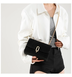 Detail of a chic black matte crossbody bag with a gold chain and oval metal lock