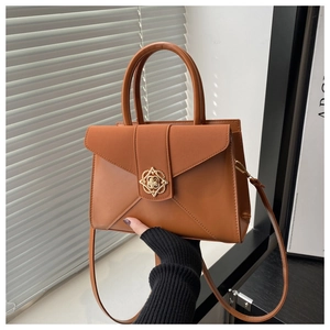 Close-up of caramel leather handbag featuring a decorative floral gold clasp and top handles