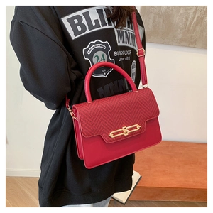 Detail of red crossbody bag featuring woven flap and gold metal clasp worn with black hoodie