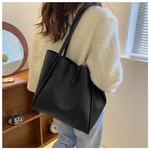Detail view of black PU leather tote bag worn by a model in a minimalist interior setting