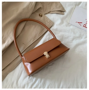 Gros plan du sac baguette en cuir caramel avec boucle dorée sur fond de tissu doux