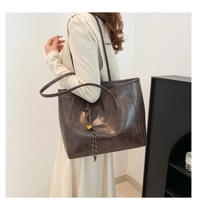 Detail of vintage oil wax leather tote bag featuring a gold bell and woven charm accessory