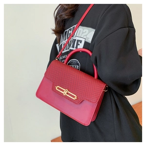 Detail of red woven texture flap and golden metal buckle on structured crossbody handbag