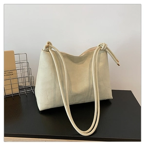 Close-up of cream tote bag with geometric embossed texture and knotted strap detail