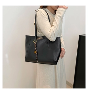 Detail of black tote bag with silk scarf charm and gold bell on model in minimalist setting