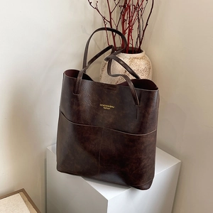 Minimalist deep brown tote bag with oily leather finish on a white geometric stand