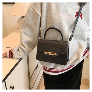 Detail of black leather handbag with lizard pattern flap and elegant gold bar metal lock