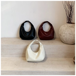 Three colors of geometric leather hobo bags on stone stairs in a minimalist setting