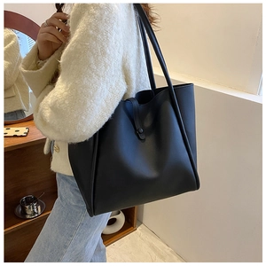 Detail of a large black leather tote bag worn by a model in a minimalist home setting