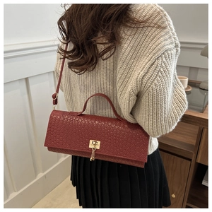 Detail of burgundy woven baguette bag with gold buckle on a model in a minimal setting