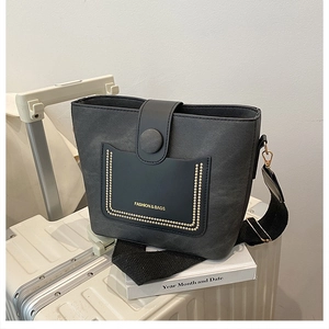 Close-up of black leather bucket bag with gold rivets and wide woven shoulder strap