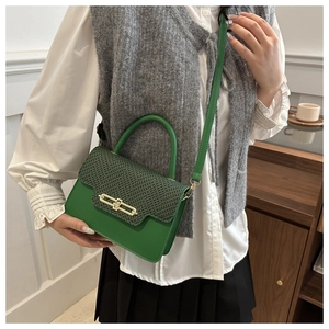 Macro shot of green textured crossbody bag with gold buckle and woven flap detail