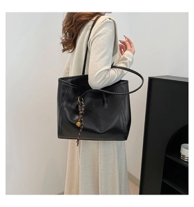 Detail of black faux leather tote bag featuring a woven tassel and golden bell charm