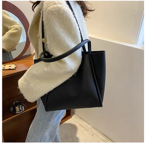 Minimalist black tote bag in matte leather shown on shoulder for daily commute style