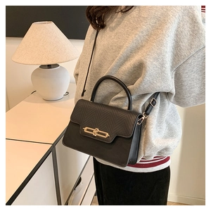 Detail of black crossbody bag featuring a golden lock and textured leather flap on model