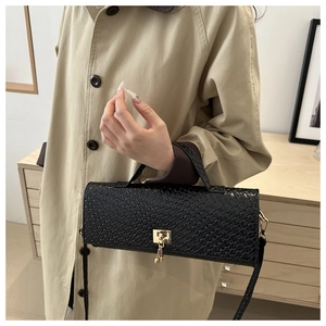 Close-up of black woven leather handbag with gold buckle held by a model in a beige coat