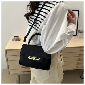 Detail of black leather crossbody bag featuring a golden oval lock and handle