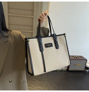 Détail d'un sac cabas en toile avec garniture en cuir noir porté par un mannequin
