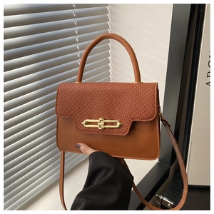 Detail of caramel leather handbag featuring embossed snake pattern and gold metal clasp