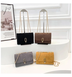Close-up of four matte suede crossbody bags with golden metal clasps and chain straps