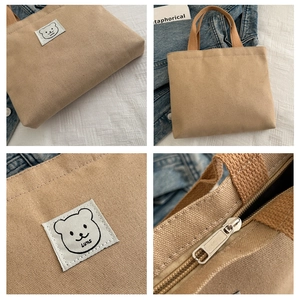 Detailed close-up of khaki canvas bucket bag featuring bear embroidery and zipper hardware