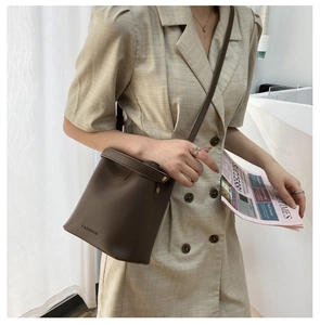 Braune Beuteltasche mit FASHION-Logo und schmalem Schultergurt am Model getragen