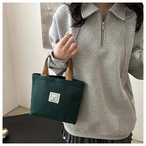 Detailed close-up of dark green canvas tote with bear embroidery and khaki straps