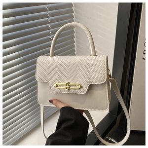 Close-up of cream white handbag featuring textured flap, gold lock and round top handle